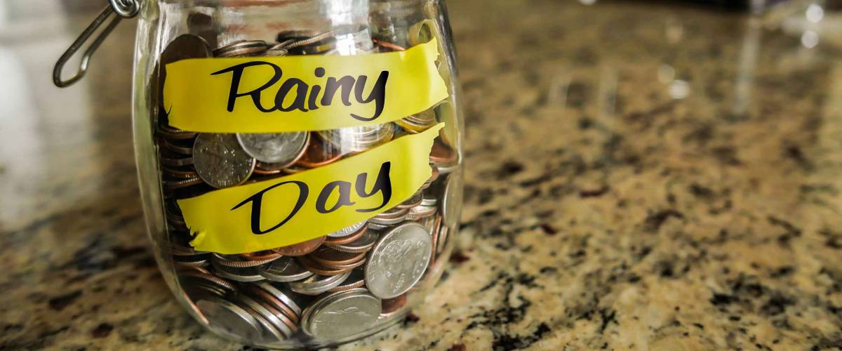 Rainy Day Money Jar. A clear glass jar filed with coins and bills, saving money. The words