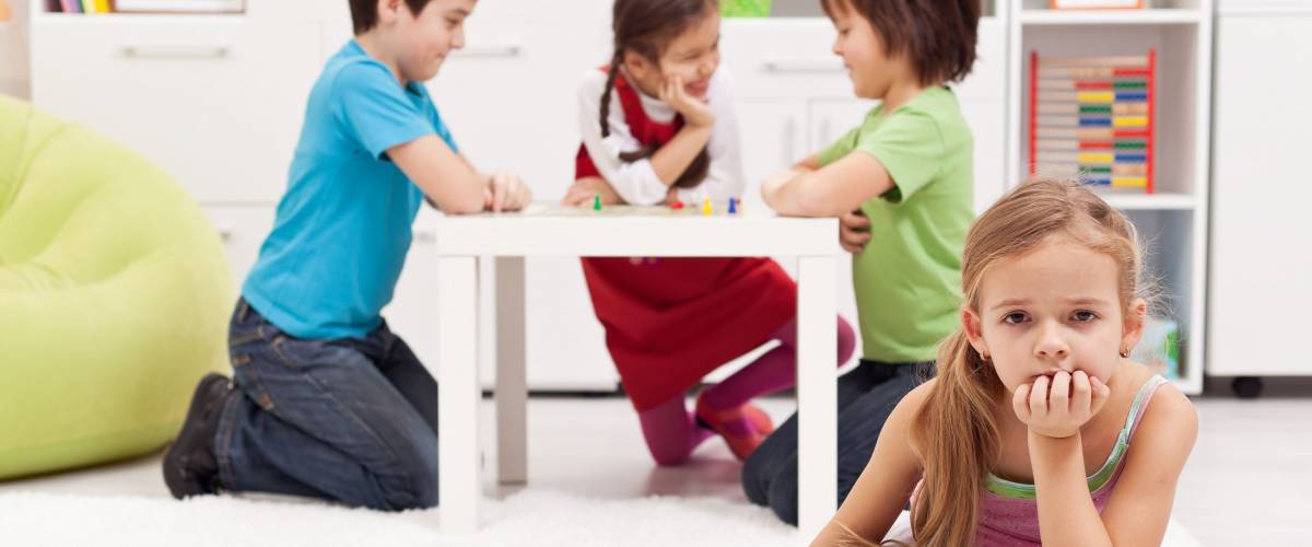 Sad girl feeling excluded from the group of playing kids