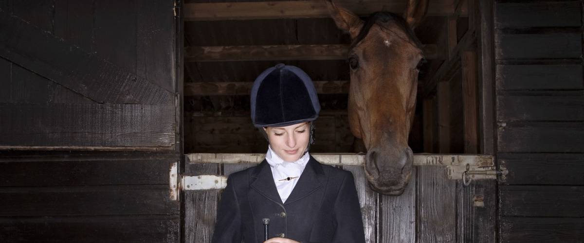 Young female horseback rider with horse and dog in the stable