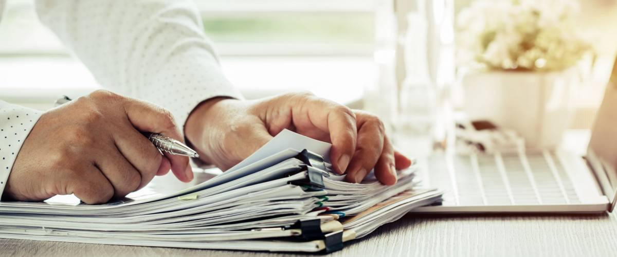 man using a pen on stacks of paper