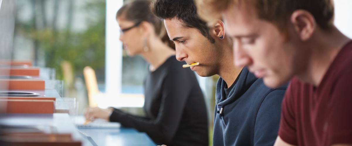 male college student sitting in library, typing on laptop computer. Horizontal shape, side view, waist up
