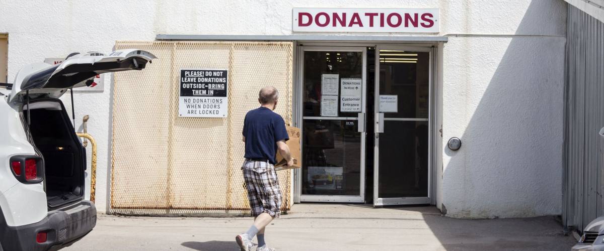 horizontal image of a man carrying donated items into a thrift store .