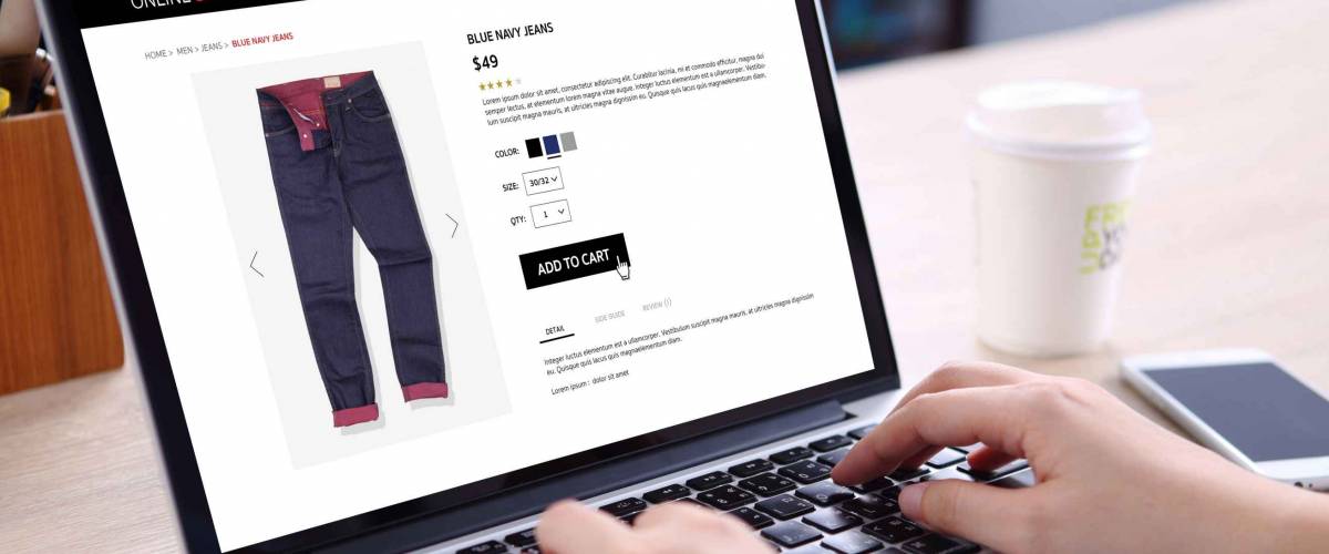 People buying blue navy jeans on ecommerce website with smart phone, credit card and coffee on wooden desk
