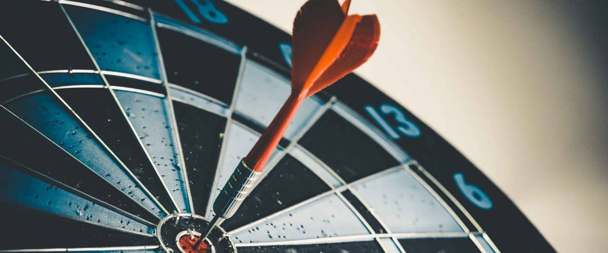 Close up shot of the dart arrow hit on bulleyes of dartboard to represent that the business reached the target of company with dark tone picture style. Target and goal as concept.