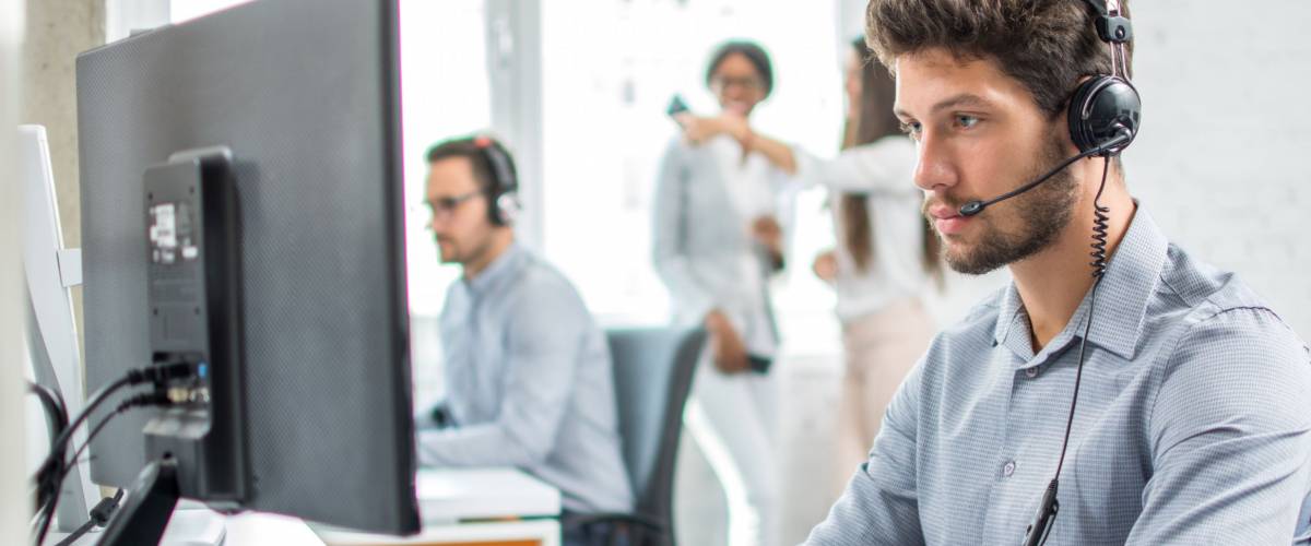 Young handsome male customer support phone operator with headset working in call center.