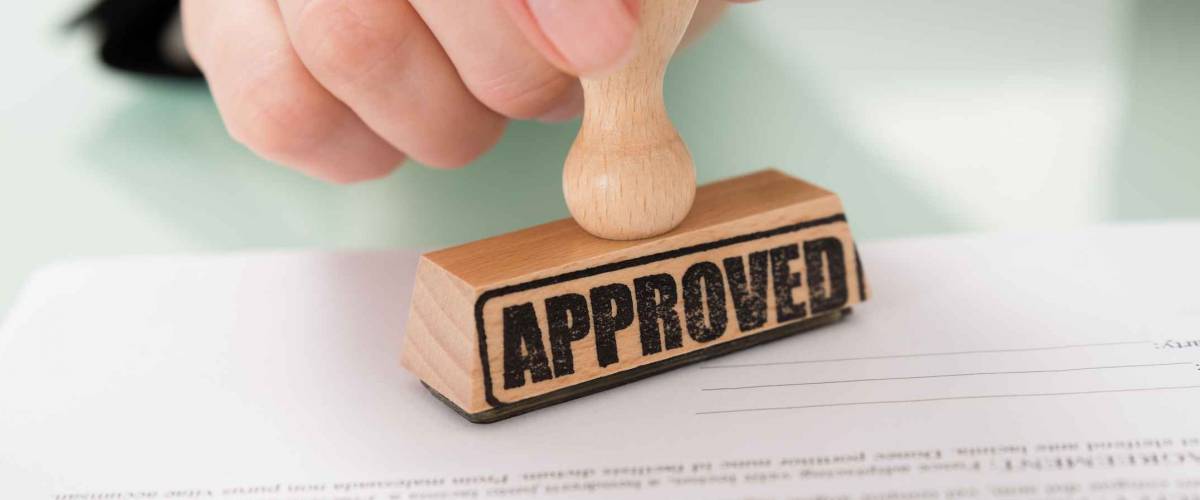 Close-up Of Businesswoman Hand Stamping Approved On Contract Paper