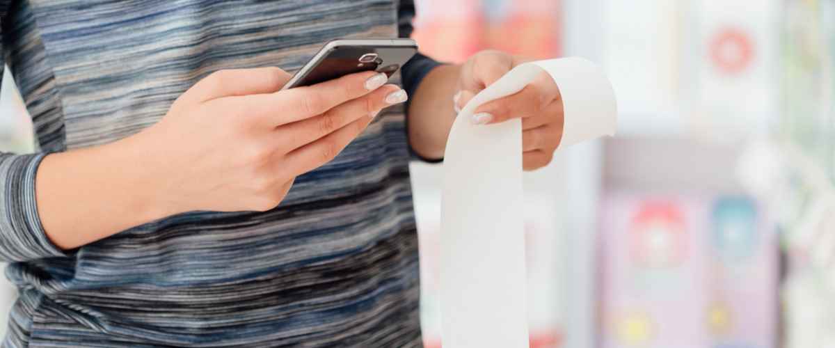 Woman holding a long grocery receipt and a smart phone