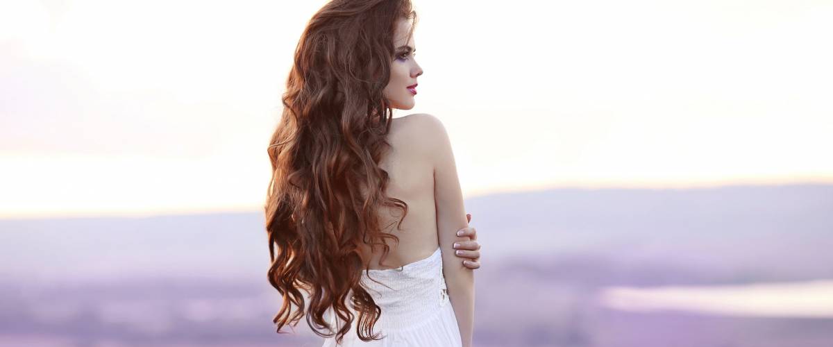 Beautiful young woman portrait in lavender field. Attractive brunette girl with long curly hair style in white dress dreaming.