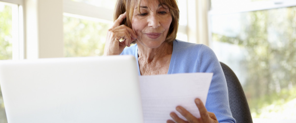 Senior woman working from home reading a piece of paper in front of her laptop