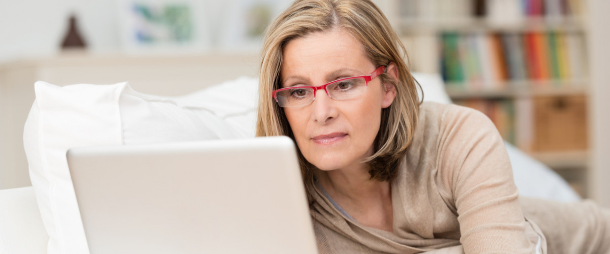 Woman on her laptop at home concentrating while lying down on her bed