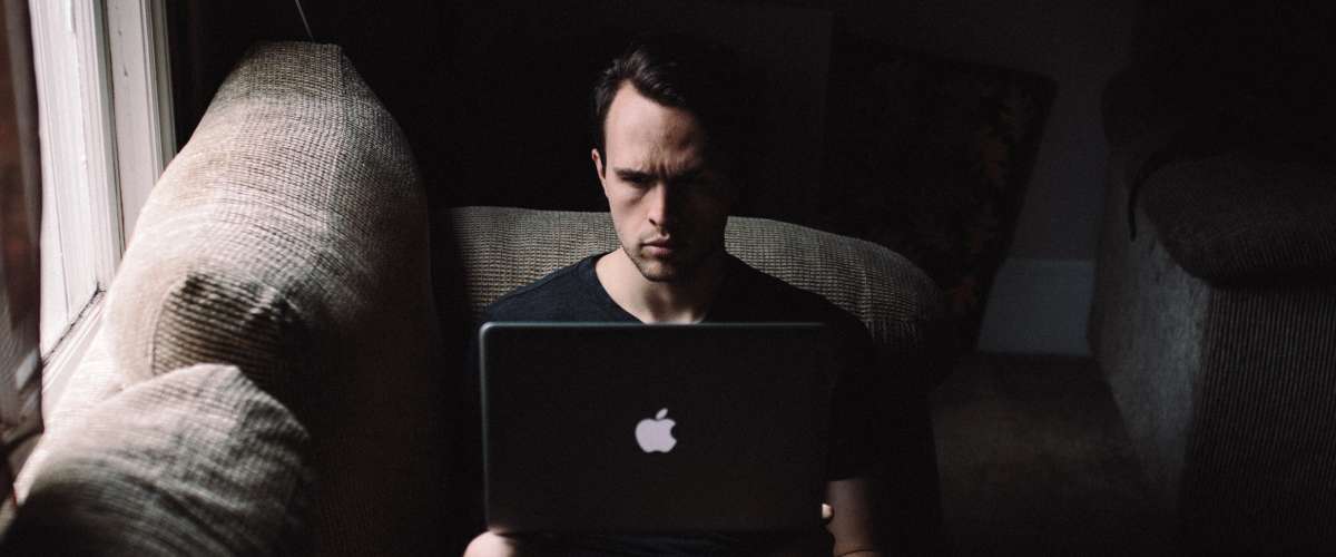 Young man working on laptop in the dark on a couch