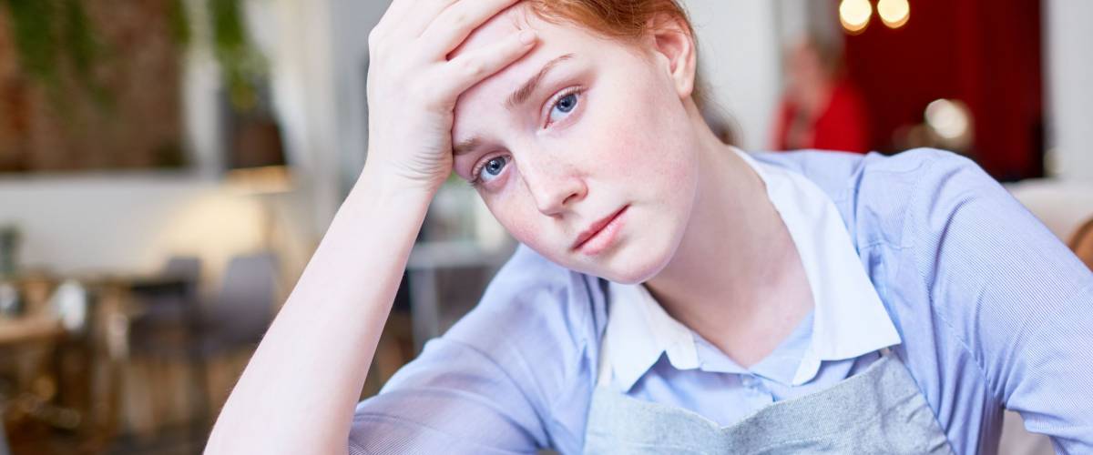 Tired and sad waitress sitting by table after work