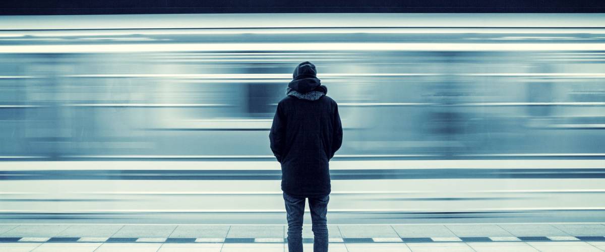 Lonely young man shot from behind at subway station with blurry moving train in background