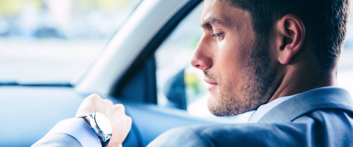 Handsome businessman looking on wrist watch in car