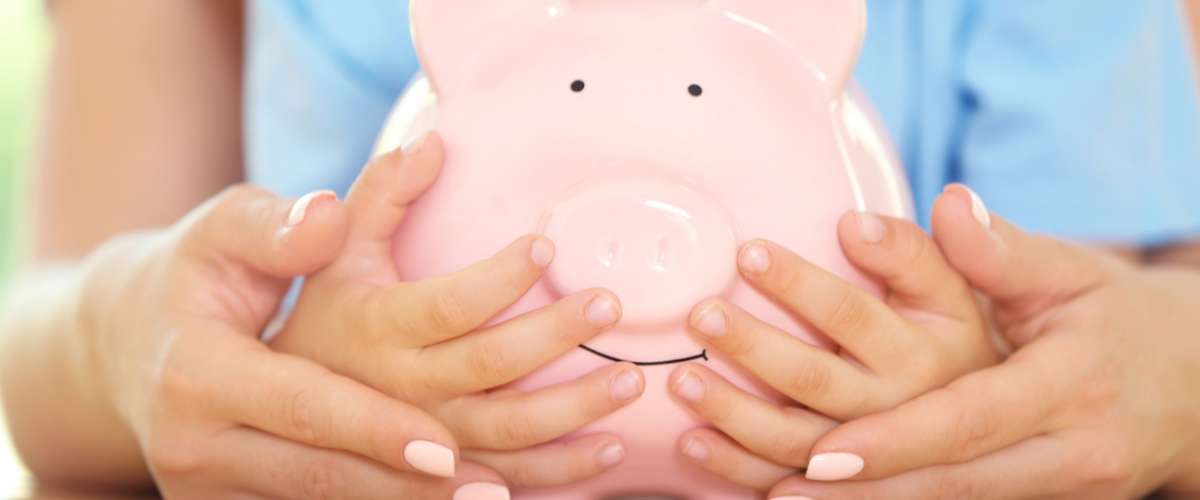 Savings concept. Mother and son hands holding piggy bank, close up