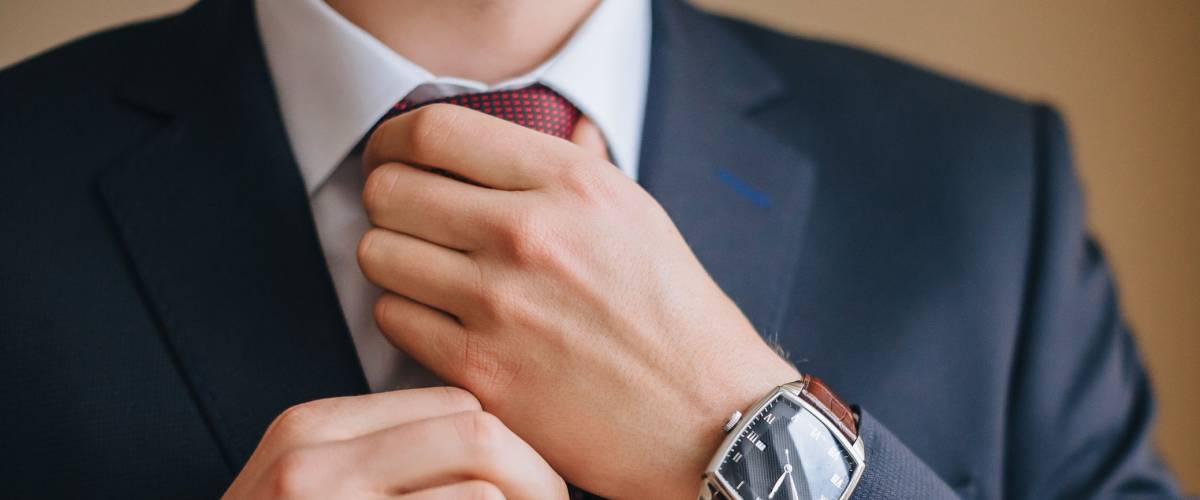 A man in a suit with a clock on his arm straightens his tie