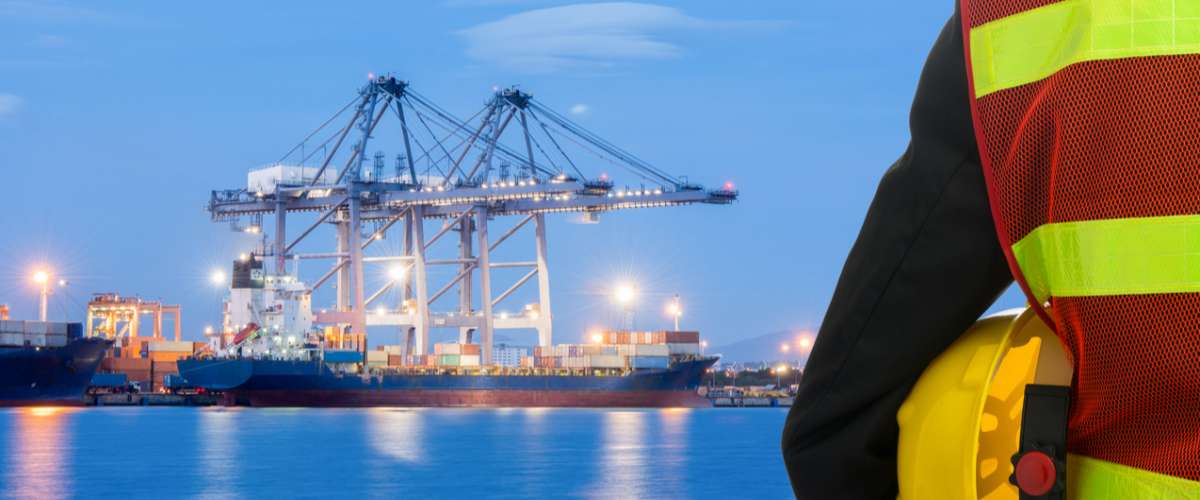 Hand or arm of engineer hold yellow plastic helmet in front of cargo port loading