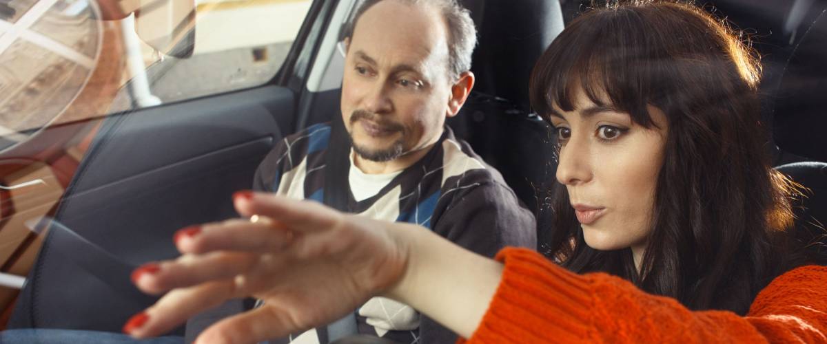 Girl in orange sweater driving with man