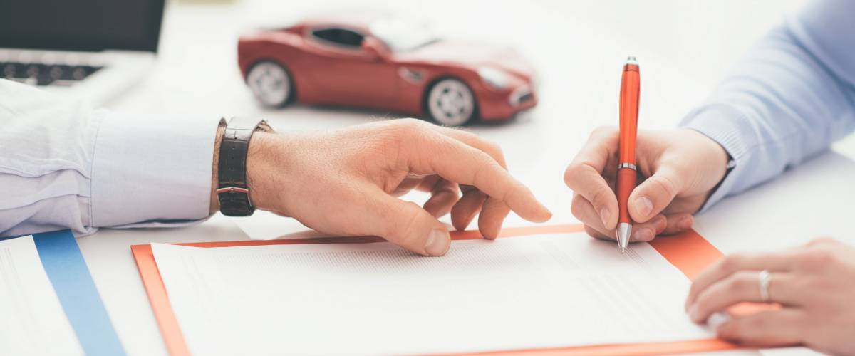 Woman signing a car insurance policy, the agent is pointing at the document