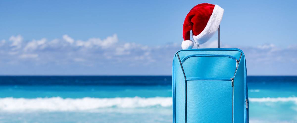Santa Claus hat on suitcase handle with tropical beach and turquoise sea background. Christmas and New Year celebration. Nobody.