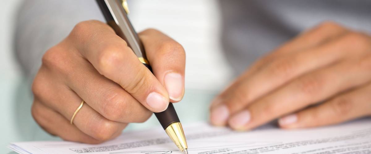 Woman at office desk signing a contract with shallow focus on signature.