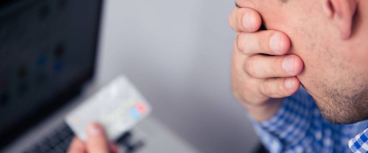 Upset man holding credit card with laptop on background