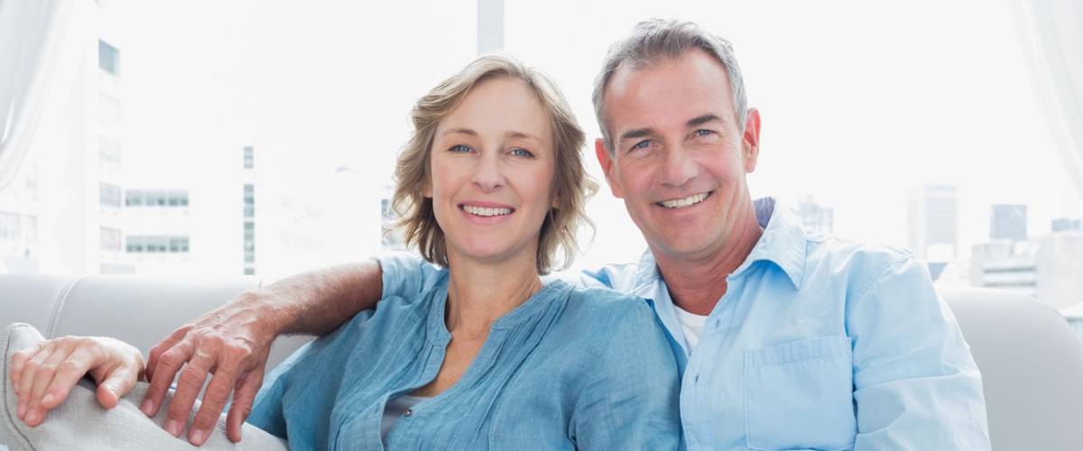 Middle aged couple relaxing on the couch smiling at camera at home in the living room