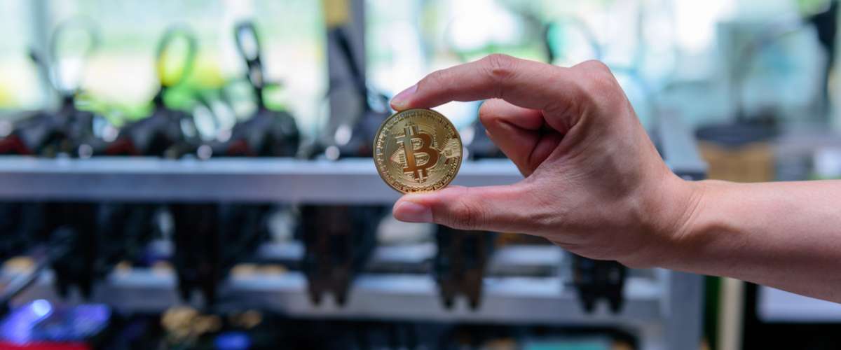 bitcoin holding in hand with mining rig computer in the background