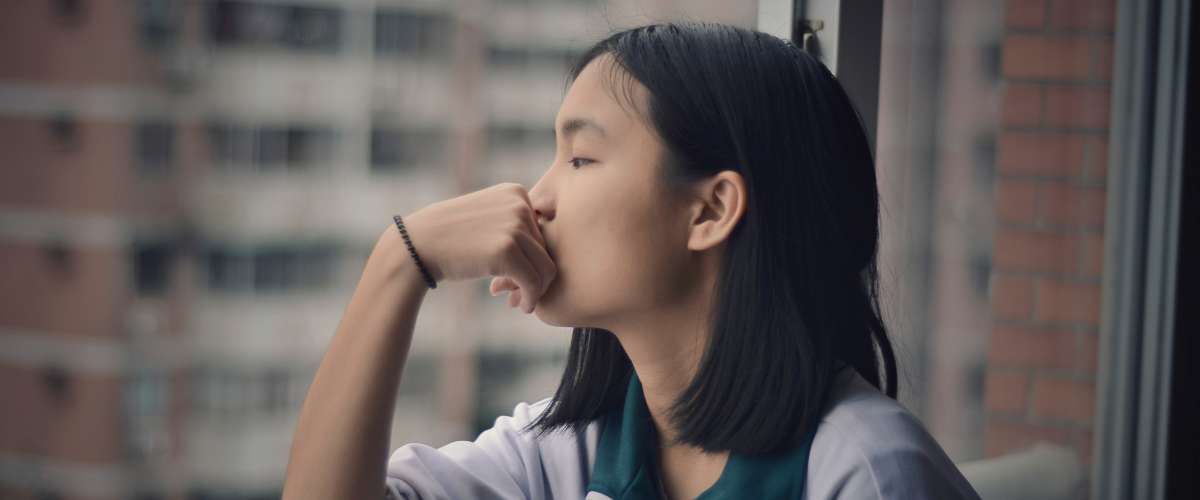 young girl looking out window in high rise pensive