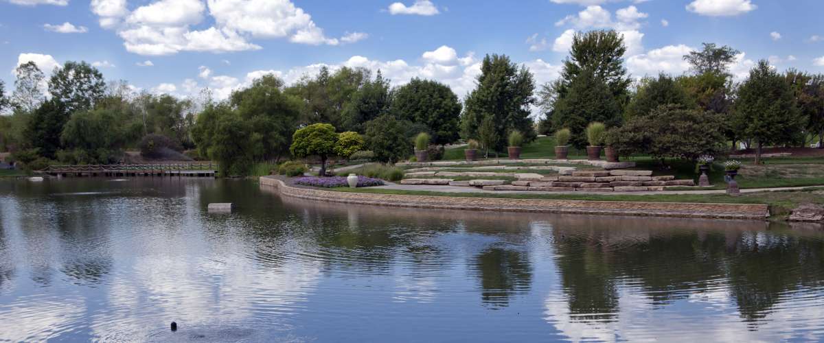 Calm waters in a large pond at the Overland Park (Kansas) Arboretum reflects fair weather cumulus clouds against a blue sky.