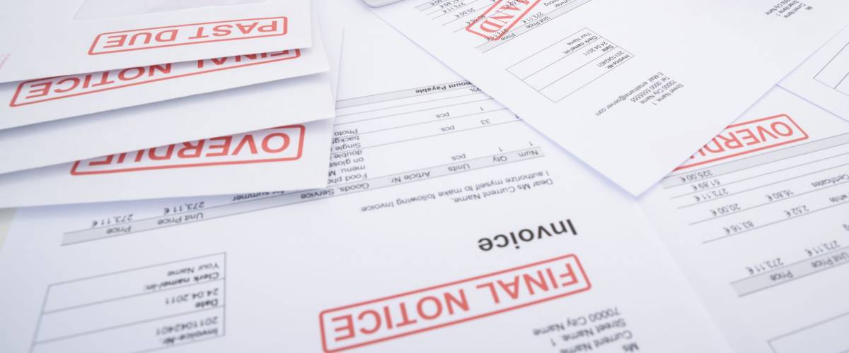 Close-up Of A Man Calculating Unpaid Bills Using Calculator