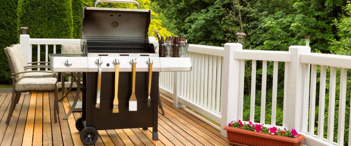 Photo of a clean barbecue cooker with cookware and cold beer in bucket on cedar wood patio. Table and colorful trees in background.