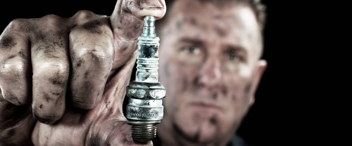 An auto mechanic shows a damaged and worn spark plug as he performs a tune up.
