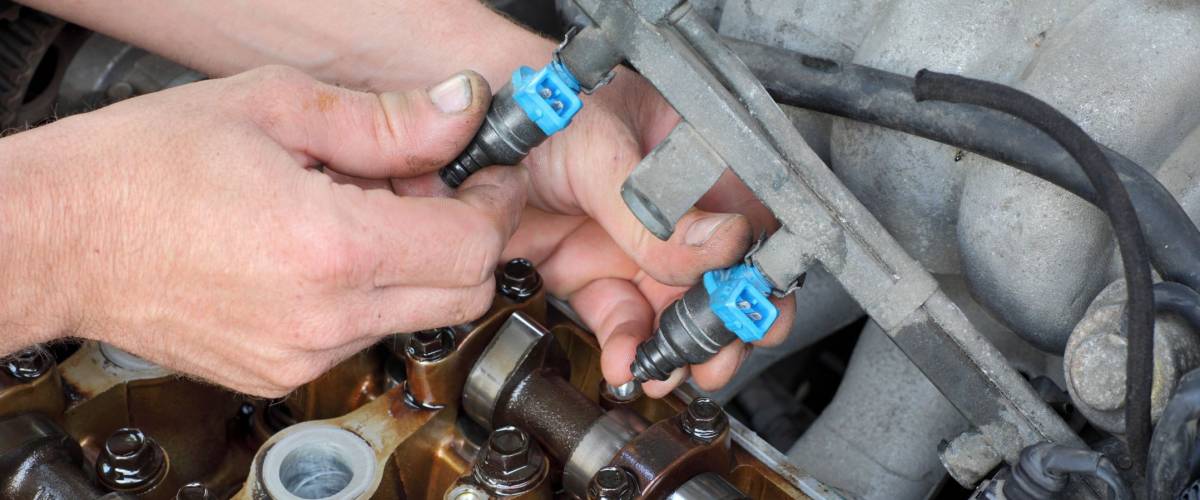 Car mechanic fixing fuel injector at two camshaft gasoline engine