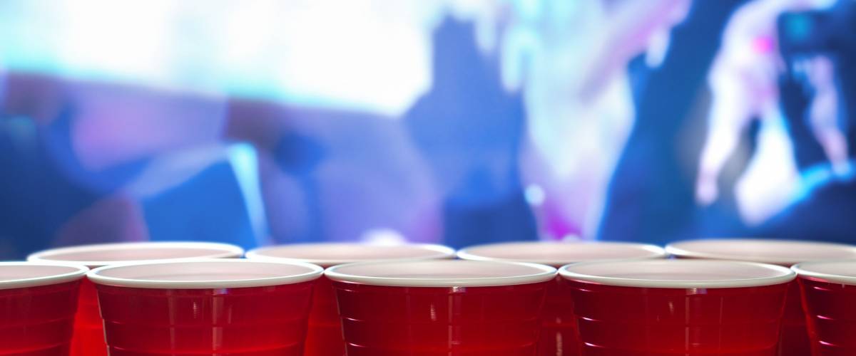 Plastic red party cups in a row in a nightclub full of people dancing on the dance floor in the background.