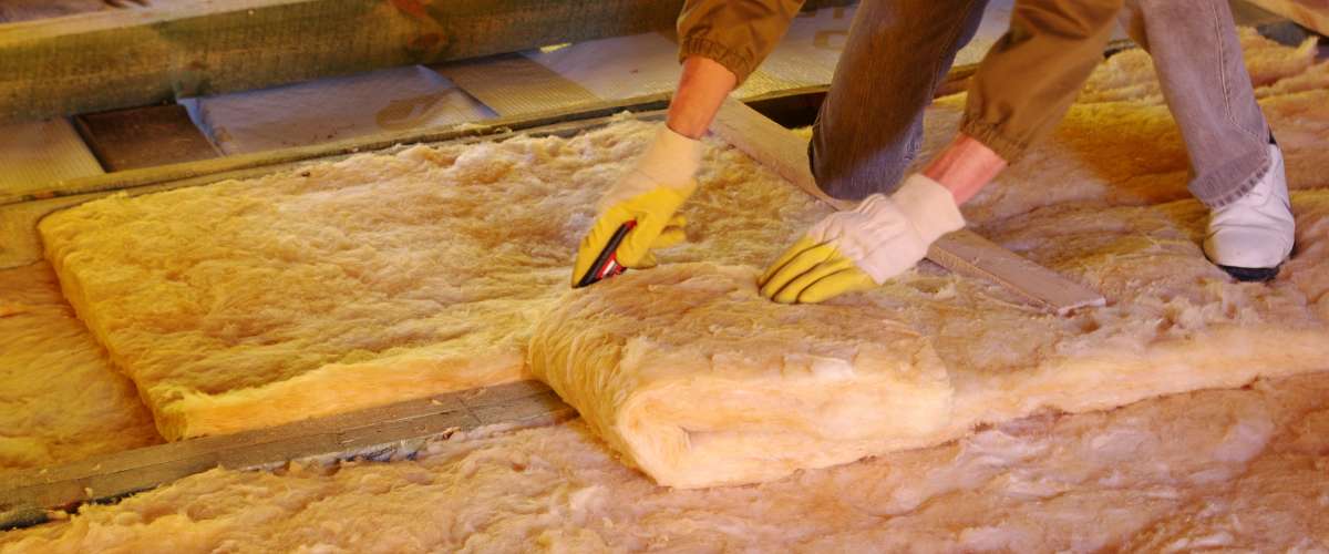 Construction worker thermally insulating house attic with glass wool