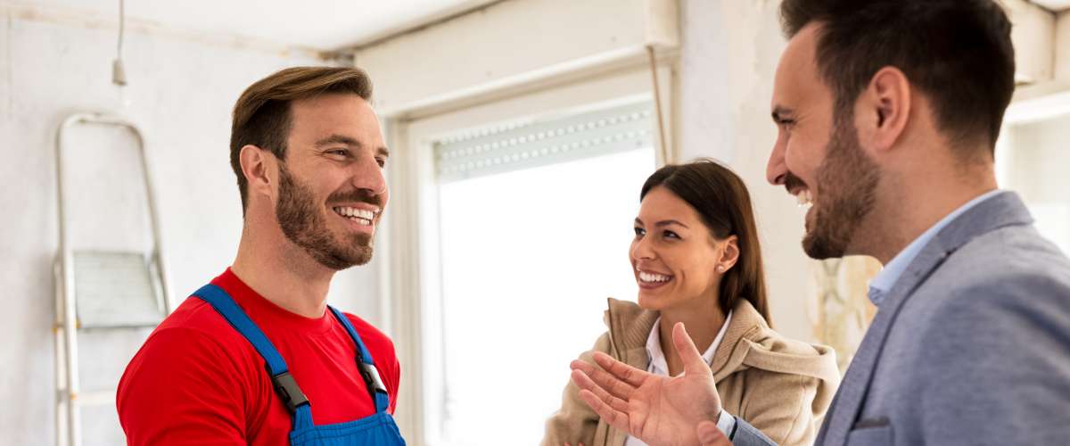 Young smiling couple and handyman talking about details of renovations home