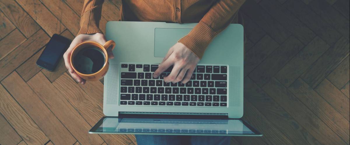 Laptop and coffee cup in girl's hands sitting on a wooden floor
