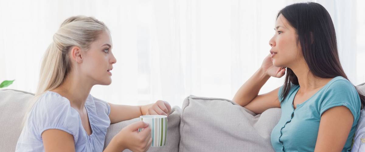 Friends drinking coffee and having a serious chat at home on the couch