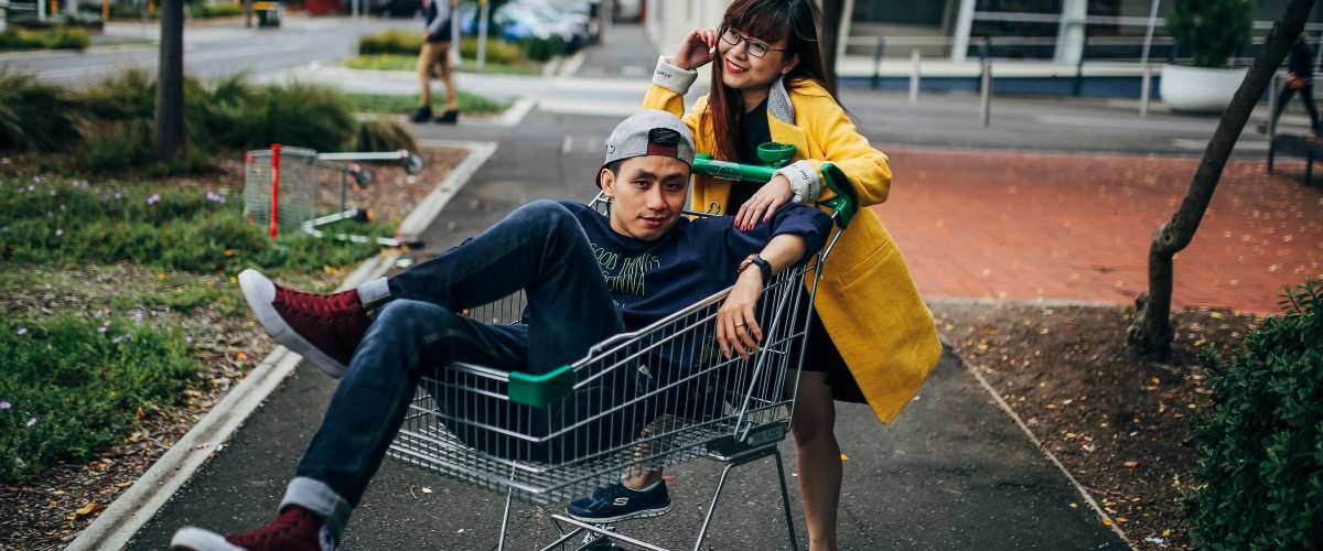 young woman pushing young man in shopping cart