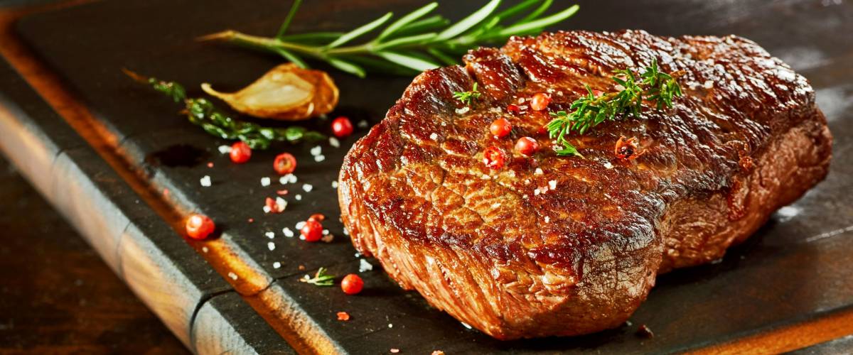 Piece of cooked rump steak with spices served on wooden cutting board