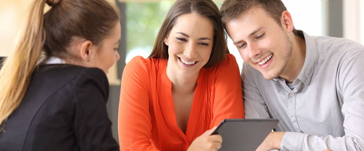 Seller showing on line products with a tablet to the customers in a desktop at office