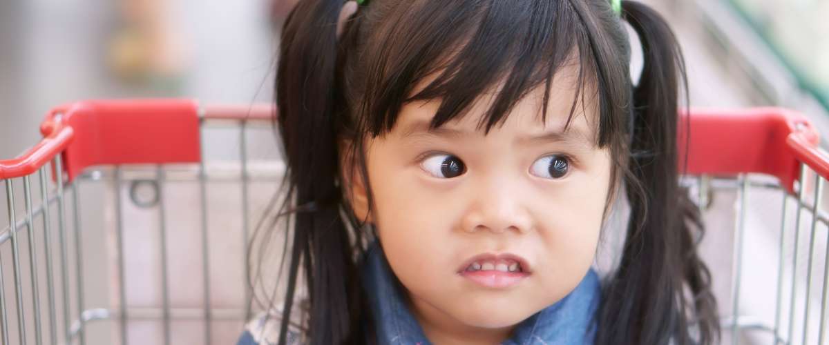 Asian children cute or kid girl wearing jeans with funny and joke or shocking face for sale price with sit in the supermarket cart at market