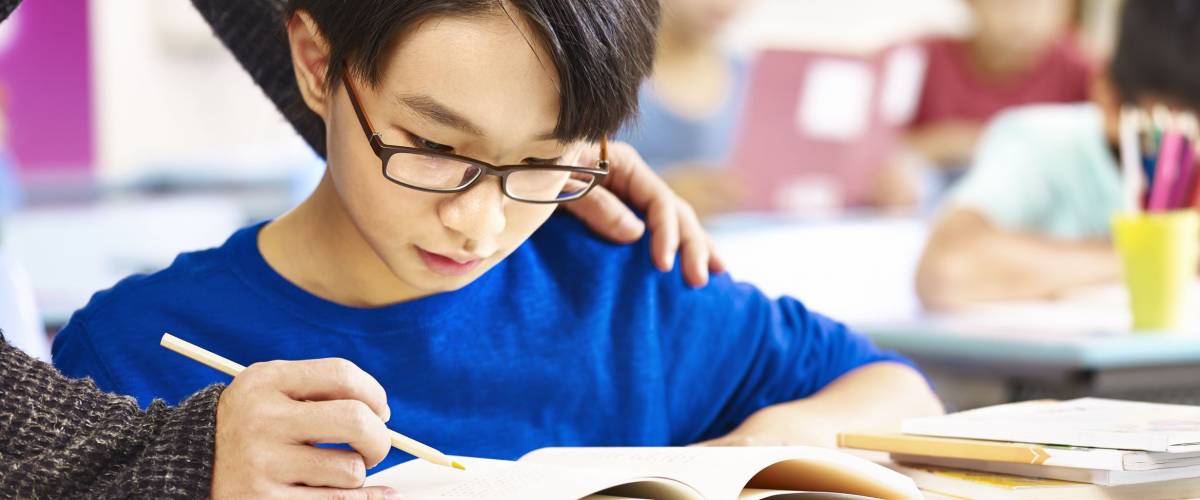 asian elementary school boy getting help from teacher in class.
