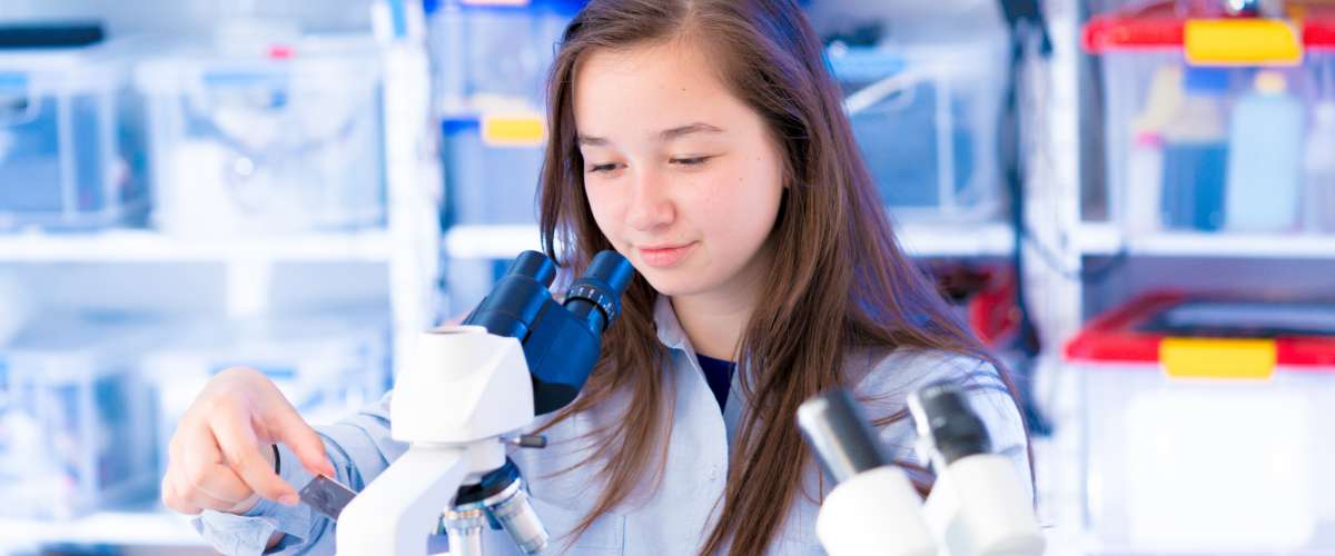 Teenager female studying science in school with microscope