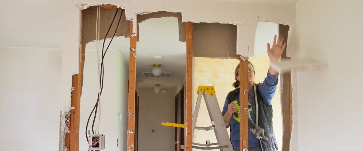 Female construction worker and homeowner using a sawsall tool to cut drywall out and take a wall down to a half-wall during a DIY house renovation.