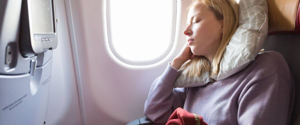 Tired blonde casual caucasian woman sleeping on seat while traveling by airplane on long distance transatlantic flight. Commercial transportation by planes.