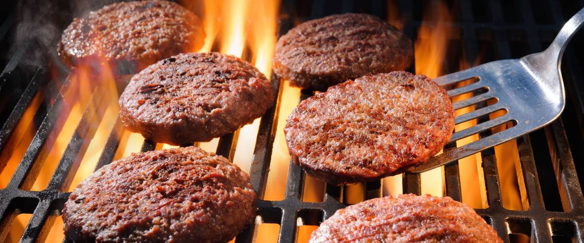 Juicy beef hamburger patties sizzling over hot flames on the barbecue