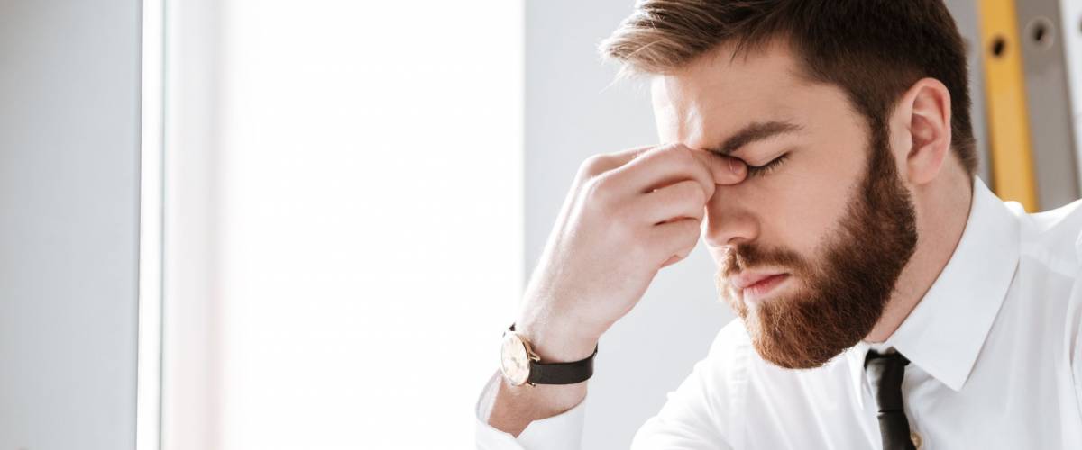 Photo of bored young businessman sitting in office near computer and glasses.