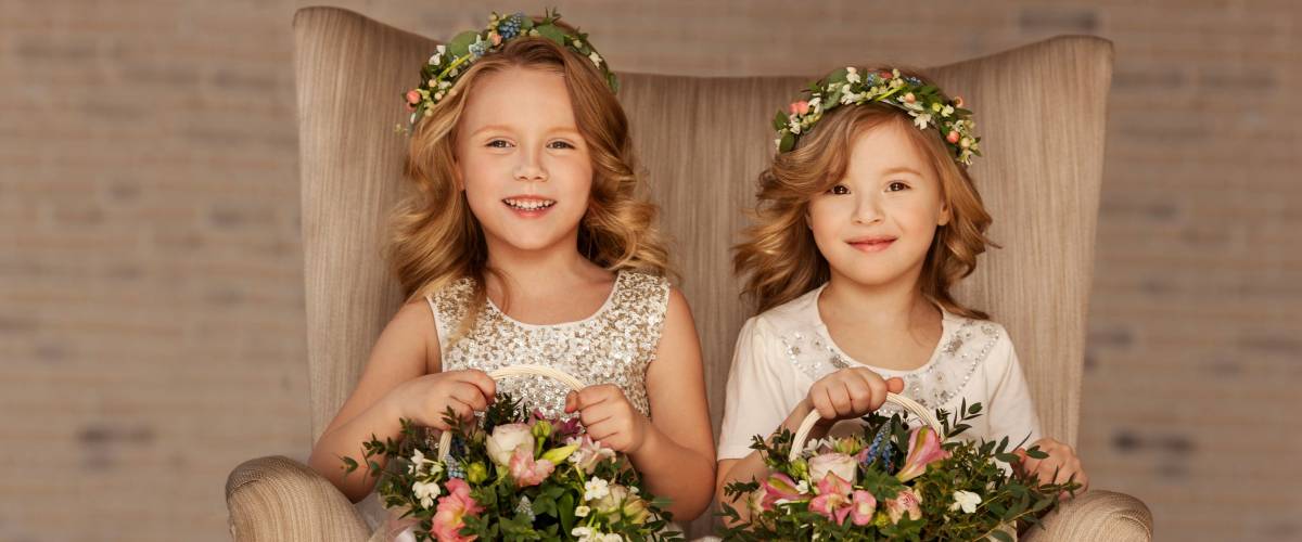 Two little flower girls sitting in a chair with bouquets